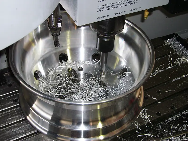 Polished metal rim being machined on a CNC bed with swarf